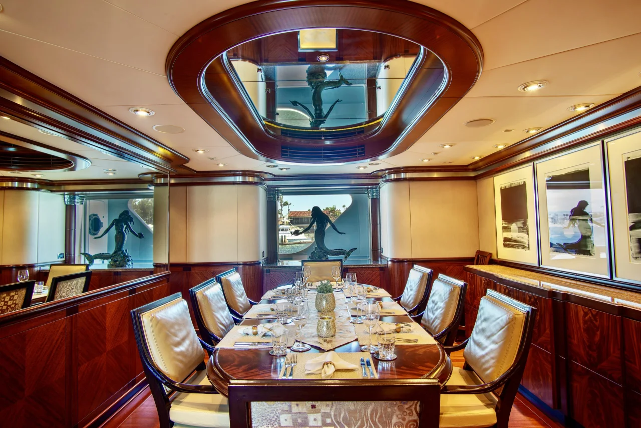 Long set dining table with upholstered chairs in a wood-paneled yacht interior